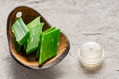 Görüntü, aloe vera yapraklarını ve aloe posasını açık renkli arka planda küçük parçalar halinde gösteriyor.