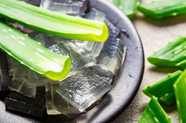 The image shows aloe vera leaves and aloe pulp in small pieces, on a light-colored background