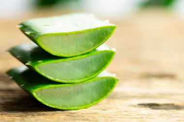Aloe vera bitkisinin resimlerinde ve ahşap bir arka planda hamurunun küçük parçalarını görebilirsiniz.