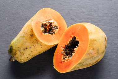 Papaya meyvesi ikiye bölündü, tohumları gri bir sayfaya serpildi.