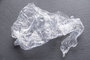 Resimde, siyah bir tahtanın üzerinde buruşmuş ve kıvrılmış bir plastik torba görebilirsiniz.