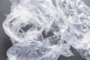 Resimde, siyah bir tahtanın üzerinde buruşmuş ve kıvrılmış bir plastik torba görebilirsiniz.