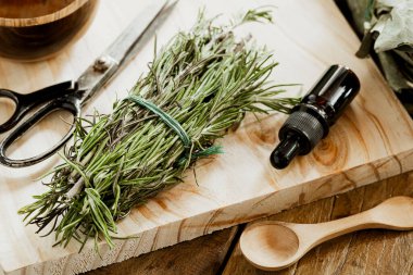 Resimde bir demet yaprak ve içinde ahşap bir yüzey üzerinde gerekli biberiye yağı bulunan cam bir kavanoz görülüyor.