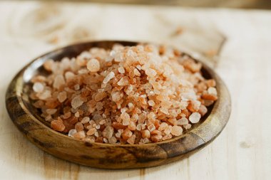 Tahta bir tabakta, ahşap bir yüzeyde pembe Himalaya tuzu yığını görülür.