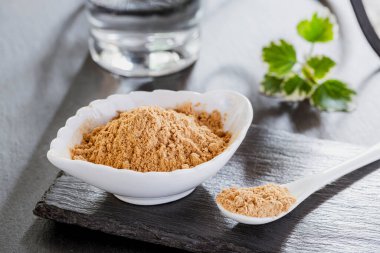 Gri bir arka planda seramik bir kapta tıbbi maca tozu.