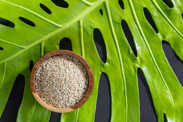 Resimde bir yığın quinua taneciği görülüyor, ahşap bir kabın içinde.