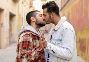 Romantic moment of a young gay couple kissing on the street touching their hands