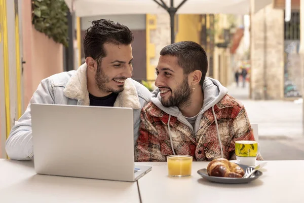 smiling gay couple at cafe using laptop