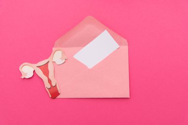 Kadın yumurtalıklarından kağıt kesiği ve pembe bir zarftan çıkan boş kart menopozu, rahim kanserini ve kadın sağlığını simgeliyor.