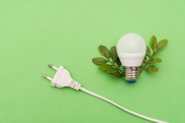 Yeşil arka planda elektrik prizi ve yeşil yapraklı LED ampul, enerji verimliliği ve çevre dostu güç