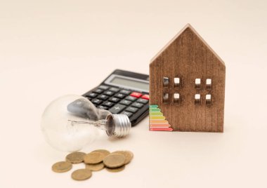 Ampul, hesap makinesi, sikkeler ve bej arka planda enerji verimliliği derecesi olan ahşap ev modeli, ev enerjisi konsepti