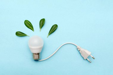 Elektrik prizli LED ampul ve mavi arka planda yeşil yapraklar çevre dostu enerjiyi temsil ediyor