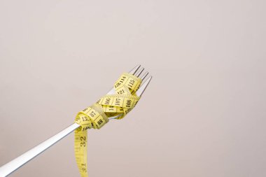 Gri bir arkaplan, diyet ve beslenme konsepti üzerinde sarı mezura ile sarılı bir Çatalın Kapanışı