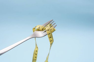 Açık mavi arka planda sarı şeritli çatal, diyet kavramı