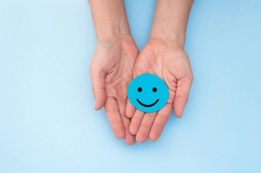 Kadının elleri gülümseyen bir yüzle mavi bir daire tutuyor, olumlu geri bildirim ve müşteri memnuniyetini temsil ediyor.