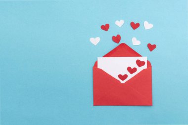 Sevgililer günü için üzerinde aşk mektubu ve mavi arka planda yüzen küçük kalpler olan kırmızı bir zarf.