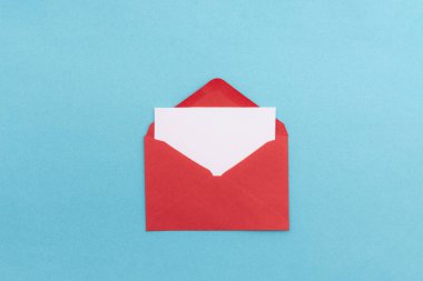 İçi boş beyaz bir kartın bulunduğu kırmızı zarf canlı mavi bir arkaplanda duruyor. Sevgililer Günü mesajlaşması için mükemmel.