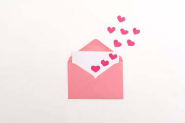 Üzerinde beyaz kart ve beyaz arka planda yüzen kağıt kalpler olan pembe bir zarf. Sevgililer günü davetiyesi.