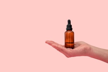 Yağ, serum veya diğer kozmetik ürünleri içeren kehribar cam damlası şişesi, fotokopi alanı ile pembe zemin üzerinde açık tutulur.