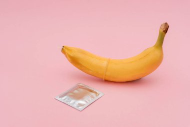 Muz üzerinde prezervatif, pembe arka planda prezervatif ambalajı güvenli seks ve doğum kontrol kavramı.
