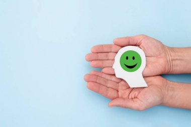 Elleriniz kağıt insan kafası ve gülümseyen emoji olumlu düşünme, iyi ruh hali, müşteri memnuniyeti ve psikolojiyi temsil ediyor.