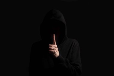 Hacker karanlık odada kapüşonlu kapüşonlu bir jest yapıyor.