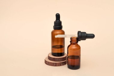Ahşap dilimler üzerinde gerekli yağ ya da serum bulunan iki kahverengi cam damlası şişesi, doğal cilt bakımı ve bej arka planda sağlık ürünleri.