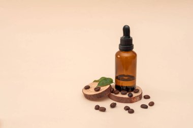 Kahveli kahve çekirdekleri, yeşil yapraklar, doğal cilt bakımı ve bej bir arka planda çevre dostu ürün konseptiyle ahşap dilimlere sergilenen kehribar düşürücü şişesi.