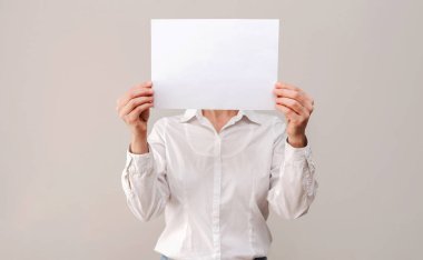 Beyaz gömlekli isimsiz bir kadın beyaz bir kağıt parçasının arkasına saklanıyor.