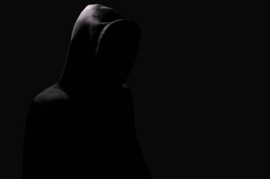 Hacker kapüşonlunun içinde saklanıyor, siyah arka plana siber saldırı düzenliyor.