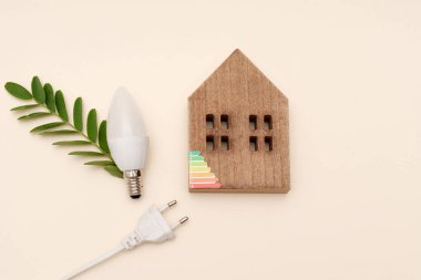 Ahşap ev modeli, yeşil yapraklı LED ampul ve tarafsız arka planda güç fişi, enerji verimliliği ve sürdürülebilir yaşam