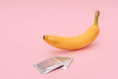 Muz, prezervatif ve pembe arka planda iki prezervatif ambalajı. Güvenli seks ve doğum kontrol kavramı.