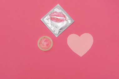 Pembe arka planda ruj, öpücük ve kalp şeklinde prezervatif ambalajı, güvenli seks ve aşk konsepti