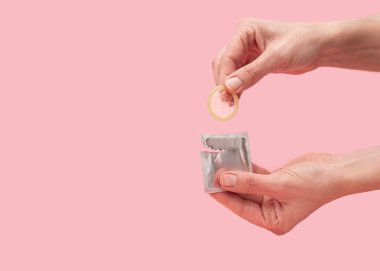 Pembe arka plan, güvenli seks ve doğum kontrol konsepti üzerindeki prezervatifi çıkarmak için ellerinizi kapatın.