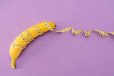 banana with yellow tape measure on purple background, loss weight or men penis size concept