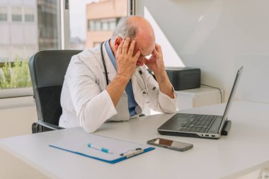 Kıdemli sıhhiyeci, tıp bürosunda dizüstü bilgisayarla çalışırken elleri, hayal kırıklıkları ve yorgunluk ile başını tutuyor.