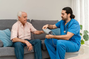 Hemşire, evdeki koltukta oturan yaşlı adamın tansiyonunu ölçüyor.