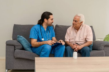 Genç erkek hemşire, sağlık desteği sağlamak için yaşlı bir adamı sağlık kontrolü için evine ziyarete geliyor.