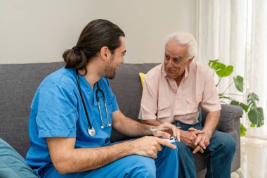 Genç erkek hemşire evde yaşlı bir adamı ziyaret ediyor. Aile içi sağlık muayenesi sırasında not alıyor.