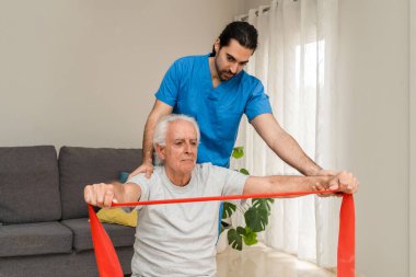 Evdeki fizyoterapistin yardımıyla direniş bandıyla rehabilitasyon egzersizleri yapıyor.