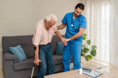 Erkek hemşire evde koltuk değneği kullanan yaşlı bir adama yardım ediyor.