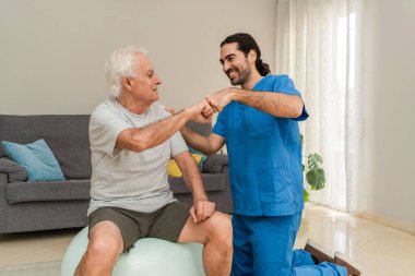 Gülümseyen erkek fizyoterapist ve kıdemli adam evdeki fitness topu egzersizlerinden sonra yumruk tokuşturuyorlar.