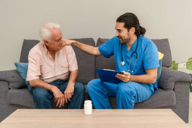 Mavi üniformalı erkek hemşire ev muayenesi sırasında yaşlı adamı rahatlatıyor.
