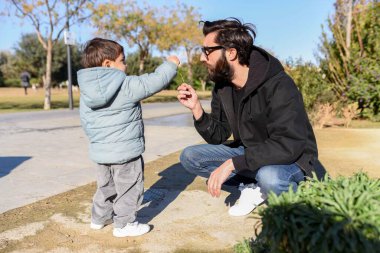 Baba ve küçük çocuk güneşli bir günde parkta oynayıp eğleniyorlar.