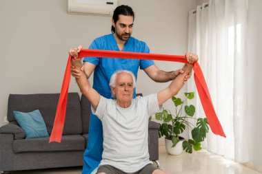Fizyoterapist, evdeki direniş bandı egzersizlerinde kıdemli adama yardımcı oluyor.
