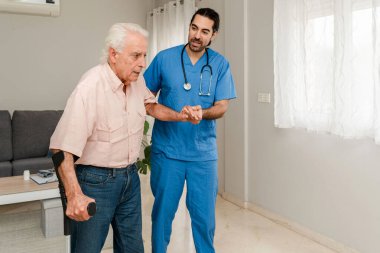 Erkek Fizyoterapist, rehabilitasyon sırasında koltuk değneği kullanan yaşlı bir adama yardım ediyor.