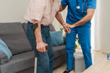 Hemşire evde koltuk değneği kullanan yaşlı bir adama yardım ederken yakın çekim yap.