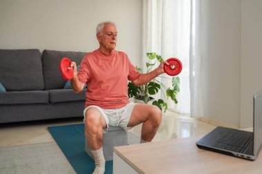 Dizüstü bilgisayardaki online eğitim programını takiben kıdemli adam evde ağırlık kaldırıyor