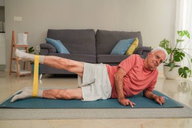 Son sınıf öğrencisi evde yoga minderinde direniş bandıyla bacak egzersizi yapıyor.