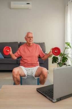 Gülümseyen son sınıf öğrencisi dizüstü bilgisayardaki beden eğitimi dersini takiben evde ağırlık kaldırıyor.